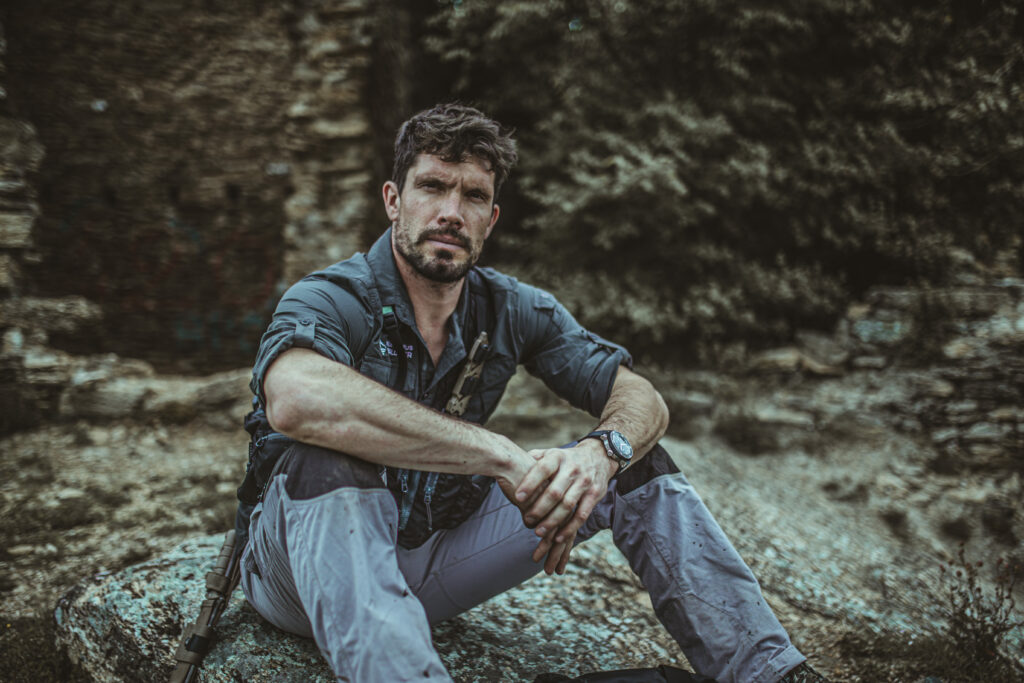 Remi Camus, an explorer, sat atop a rock and looking towards the camera.